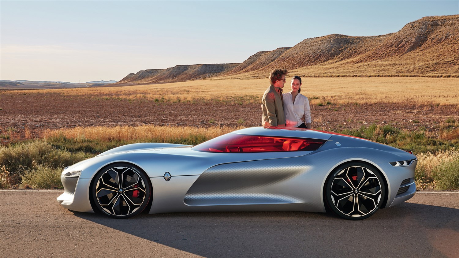 A couple standing next to Renault TREZOR concept car on the road"
